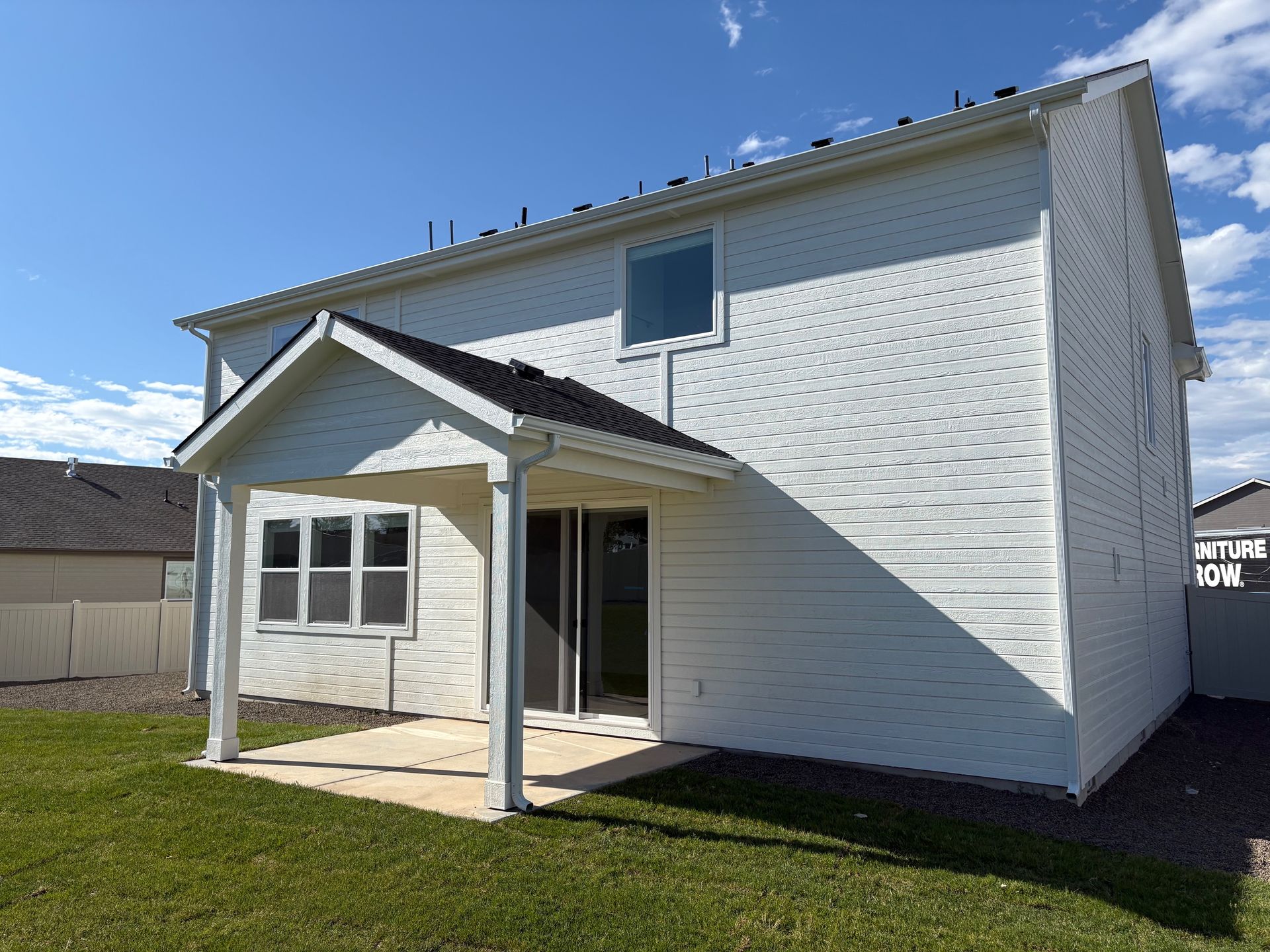 Back view of a white two-story house with a covered patio, on a sunny day.