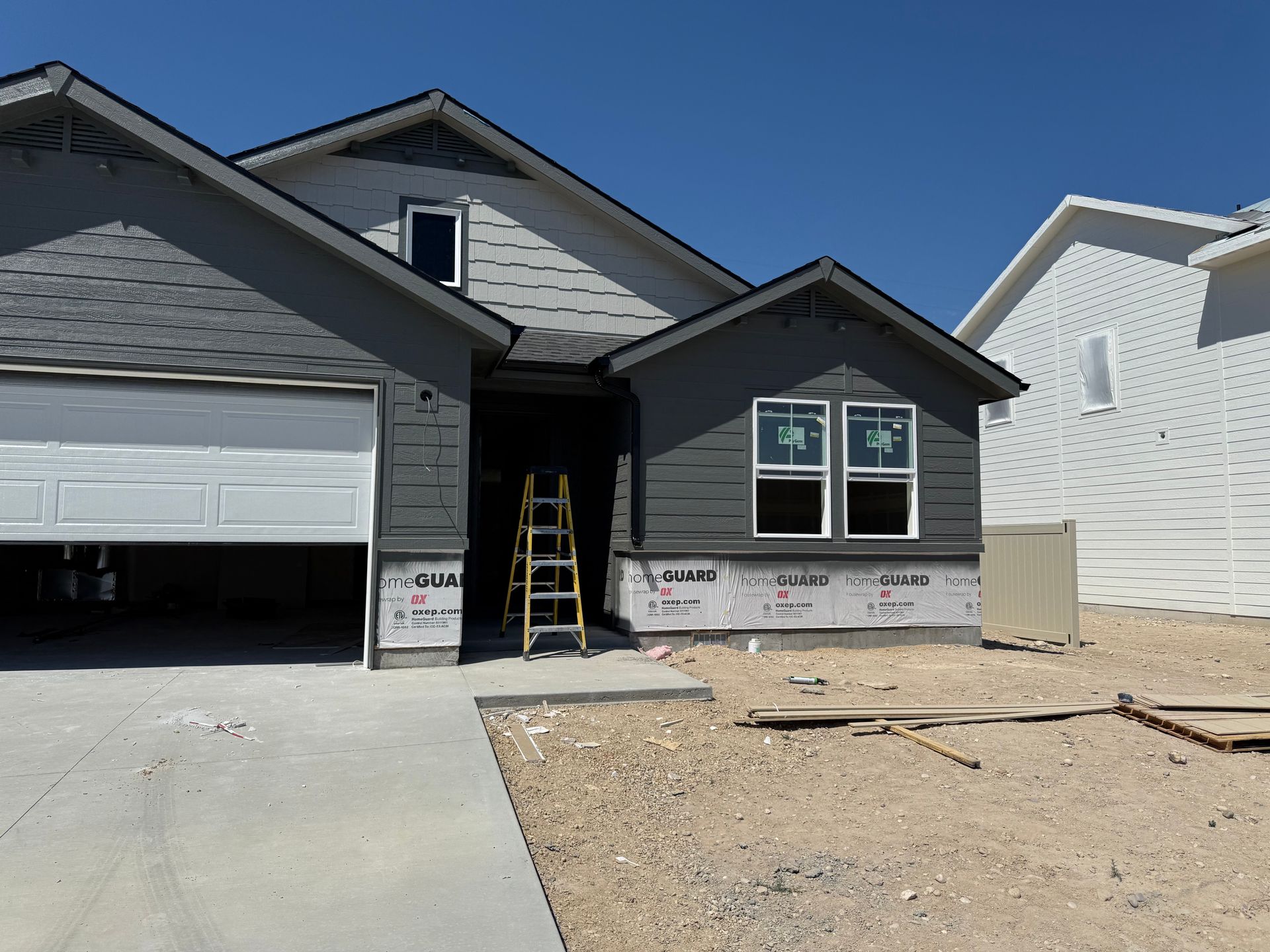 New house under construction with gray siding and an open garage door. A ladder sits in the doorway.