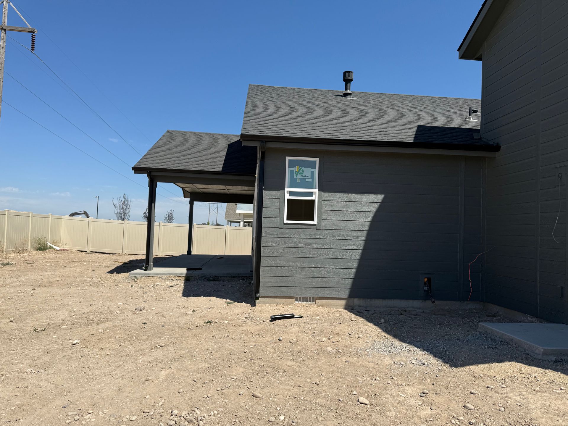 Gray house with a carport, gravel yard, and blue sky.