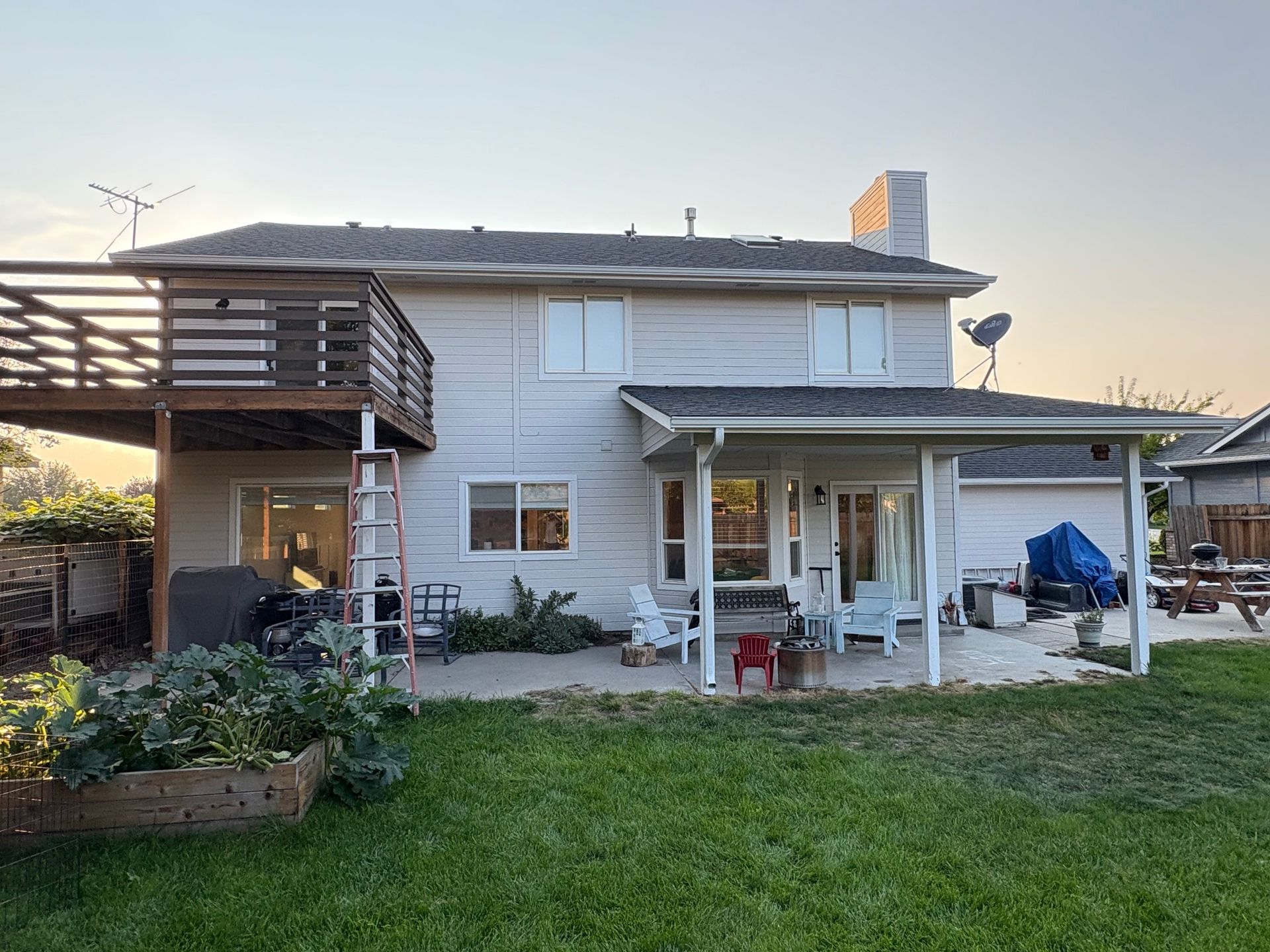 Backyard view of a two-story house with a wooden deck, patio, and raised garden bed.