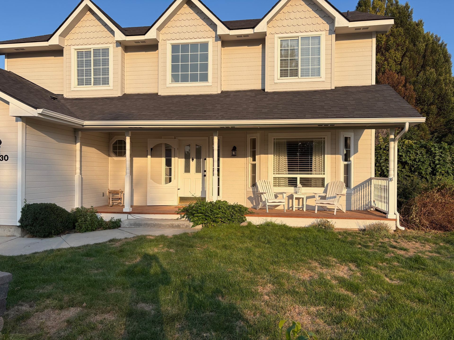 Beige two-story house with dormers, front porch, and grassy lawn.