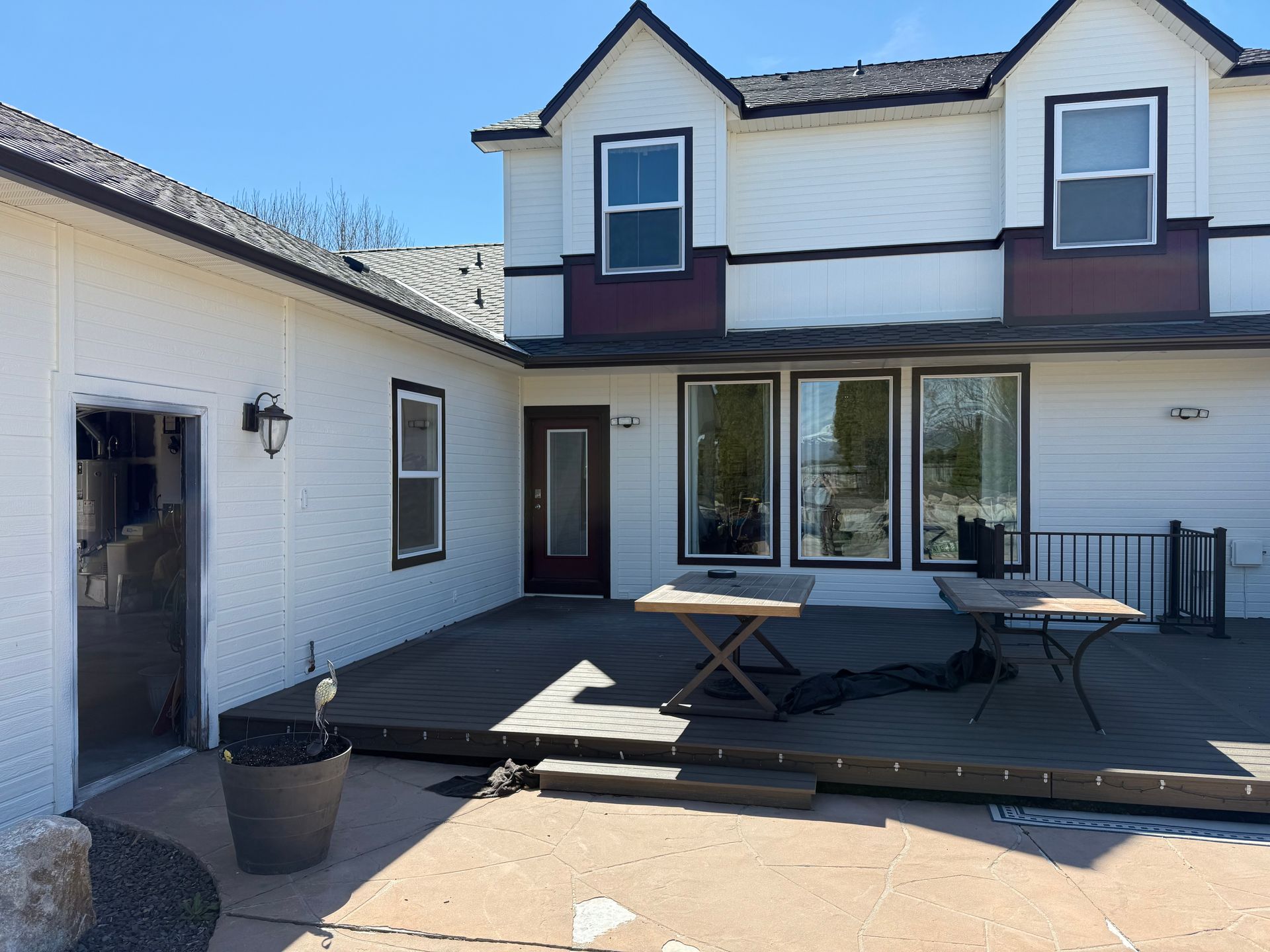 Backyard with deck, white house, and garage with open door, sunny day.