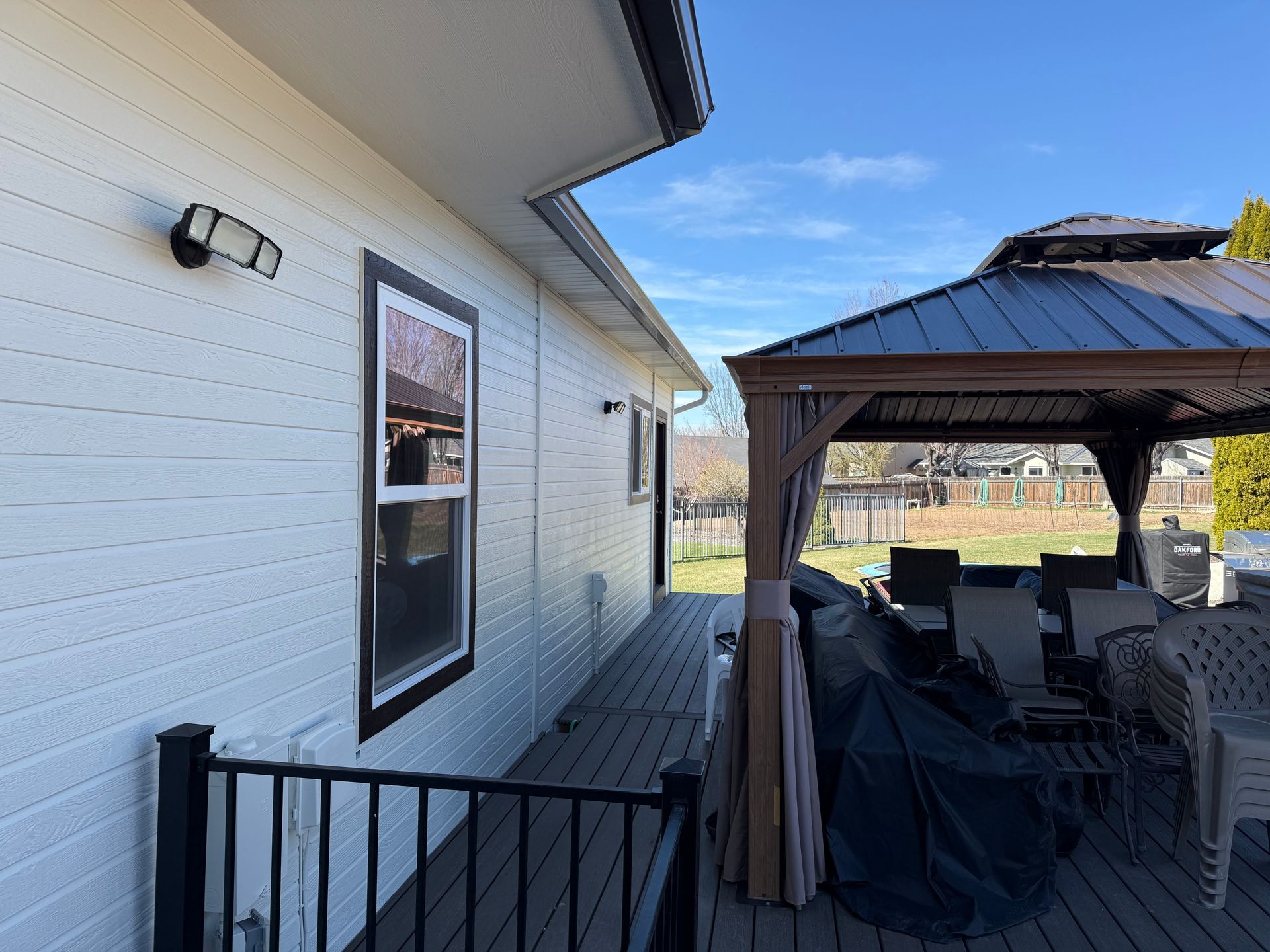 Exterior of a white house with a black-framed window and a brown gazebo on a wooden deck.