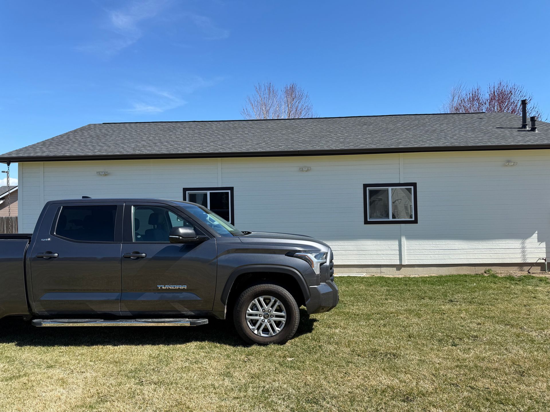Gray pickup truck parked in front of a white house with black-framed windows and a dark gray roof, under a blue sky.