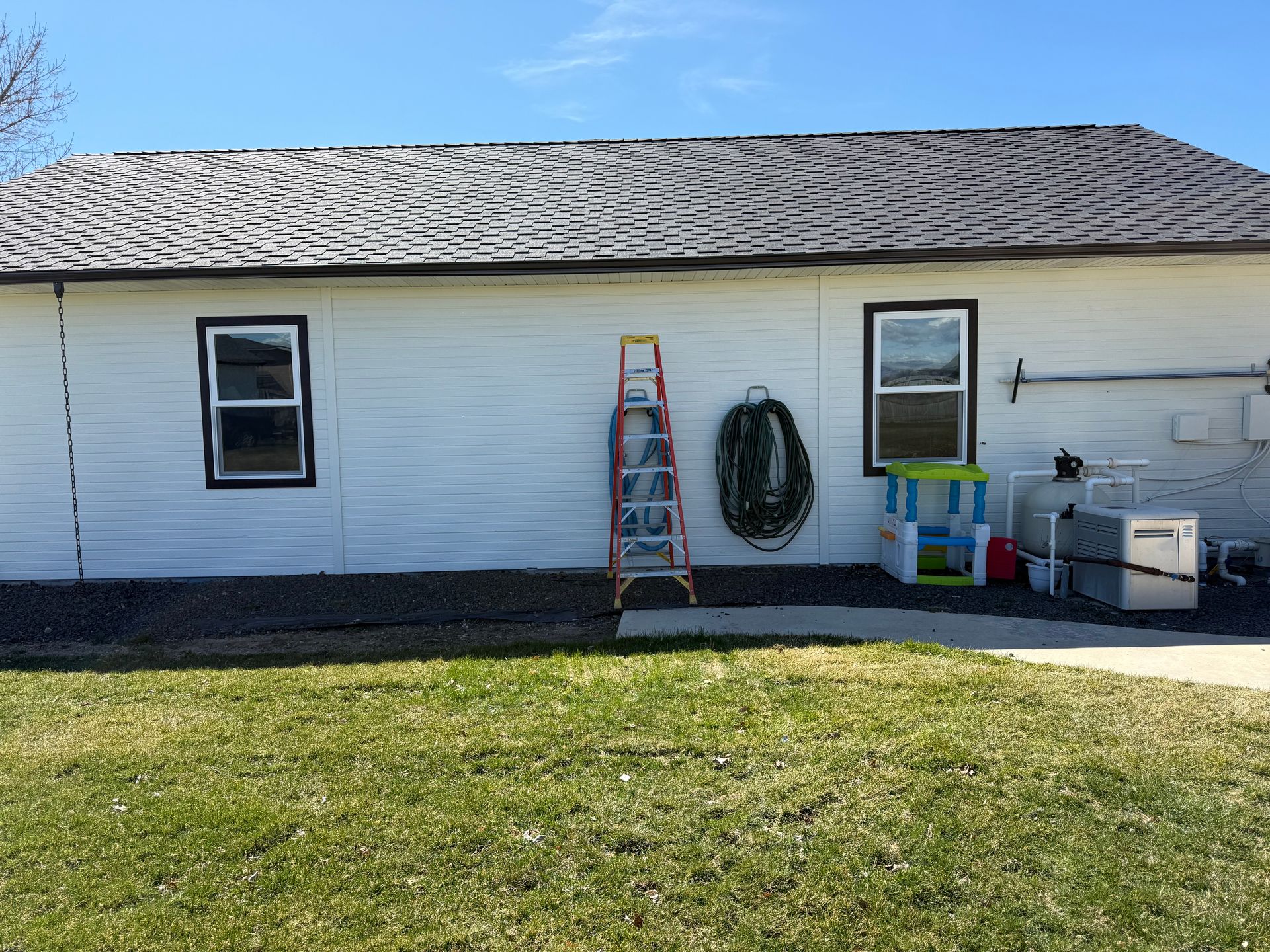 White house exterior with black-framed windows, a ladder, and a coiled hose against the wall. Green grass in the foreground.