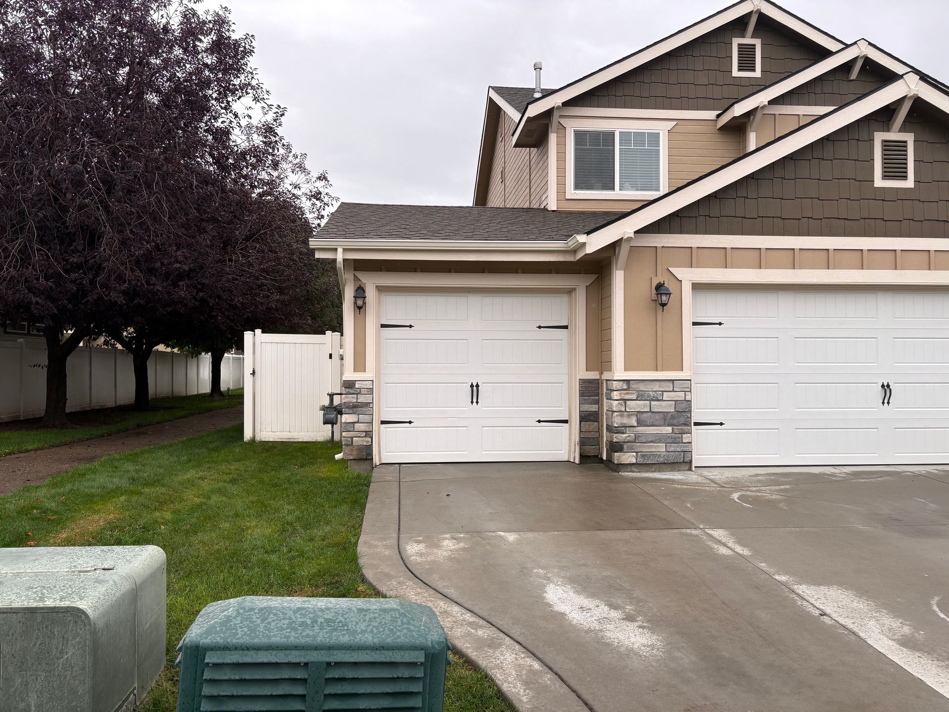 Two-story beige house with a two-car garage. A grassy lawn and concrete driveway in front.