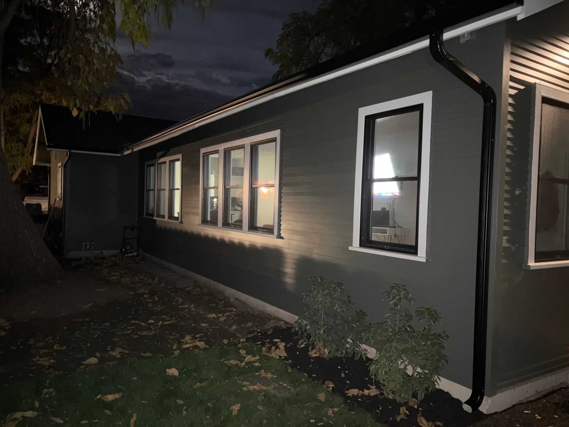 Dark green house exterior at dusk with several lit windows and black gutters.