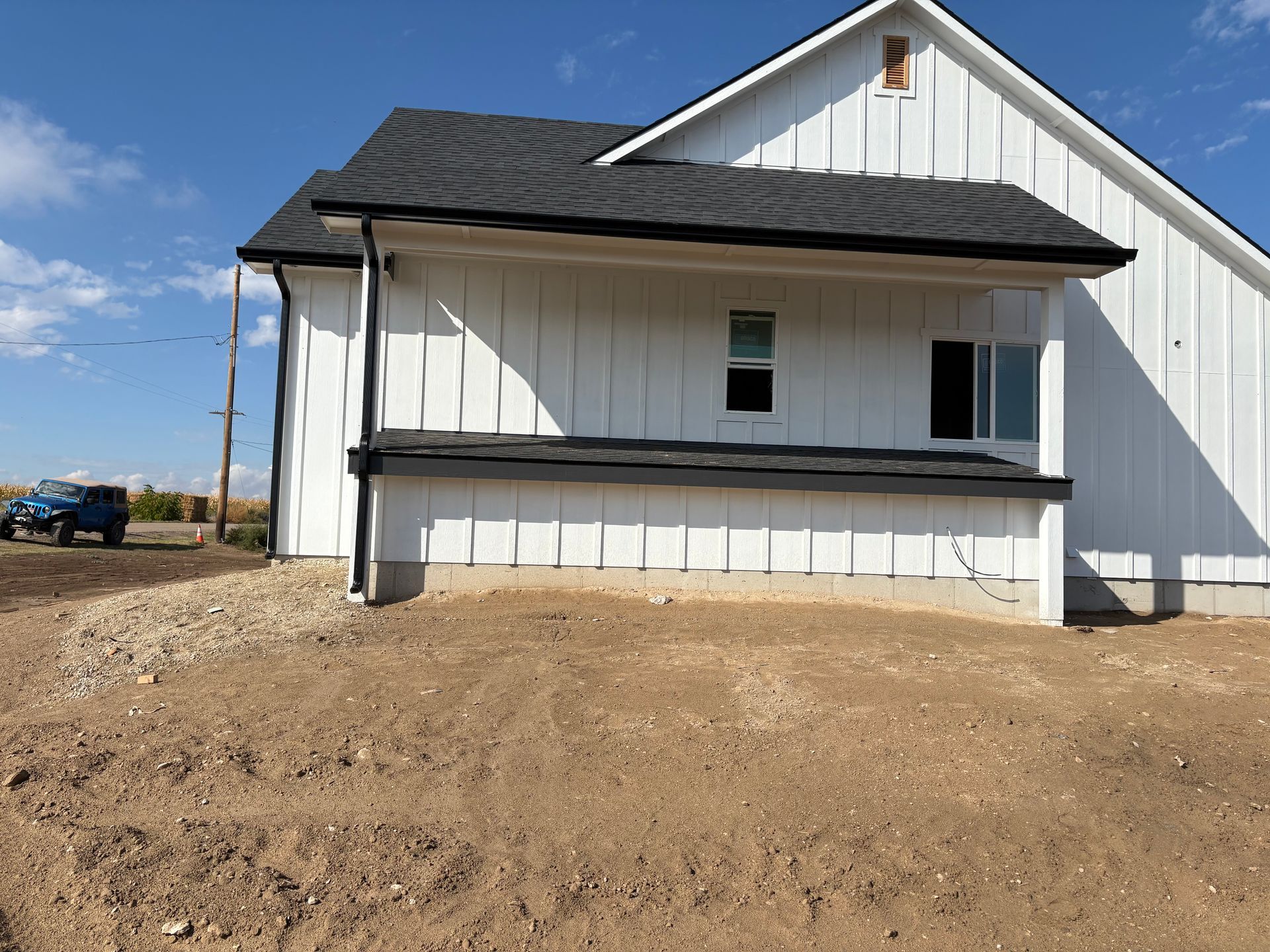 White farmhouse with black trim under a blue sky and barren land.