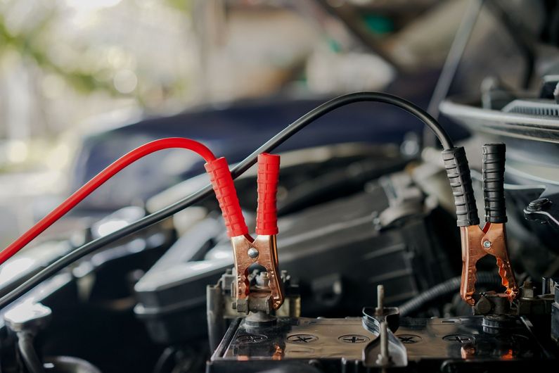 A close up of a car battery being charged with jumper cables.