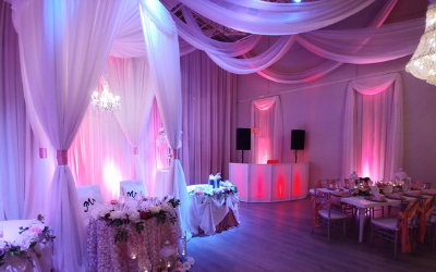 Pink-lit wedding reception hall with draped fabric, floral centerpieces, and tables set on the right