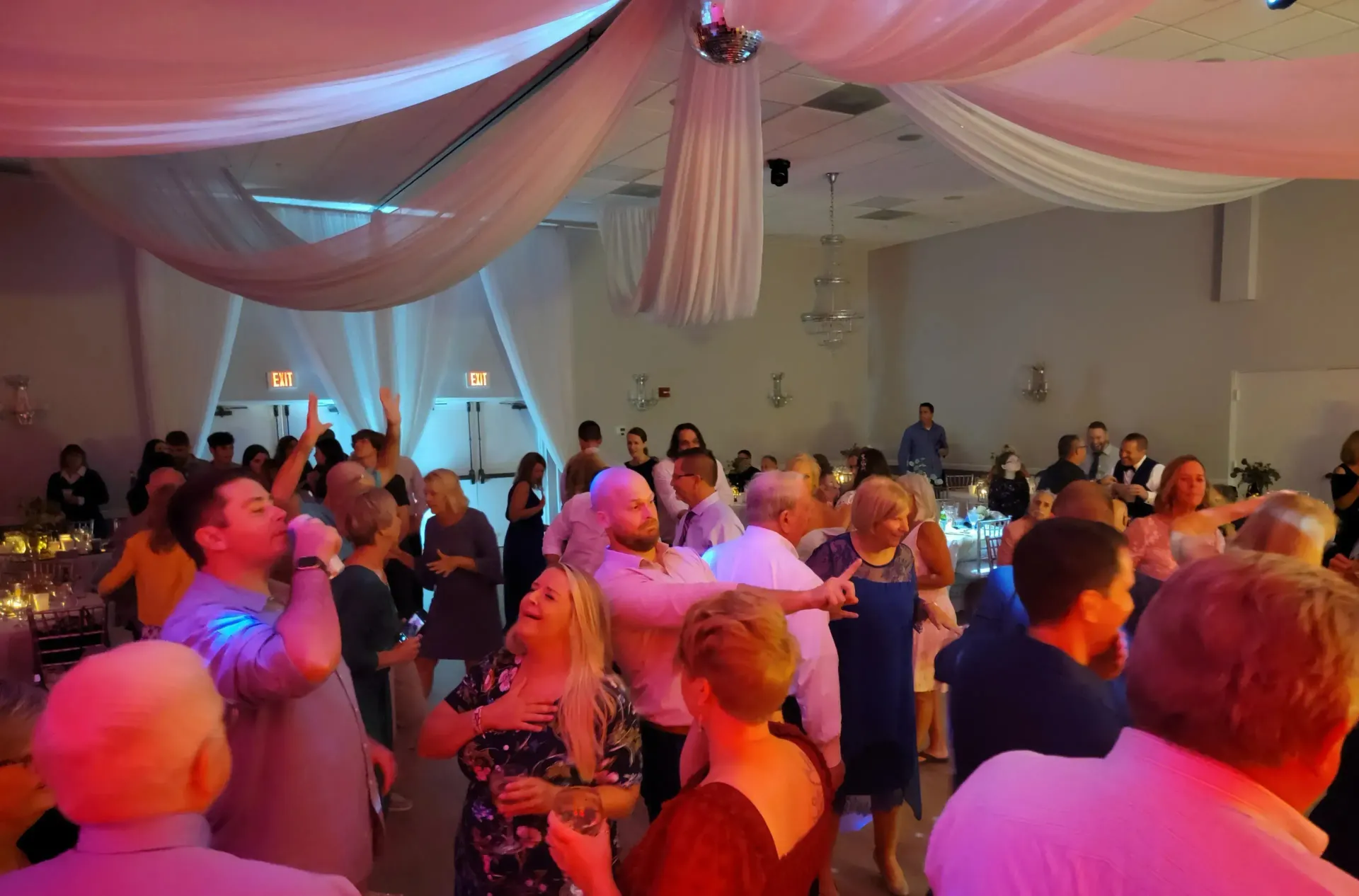 Guests mingle under pink and blue lights at a decorated indoor event hall.