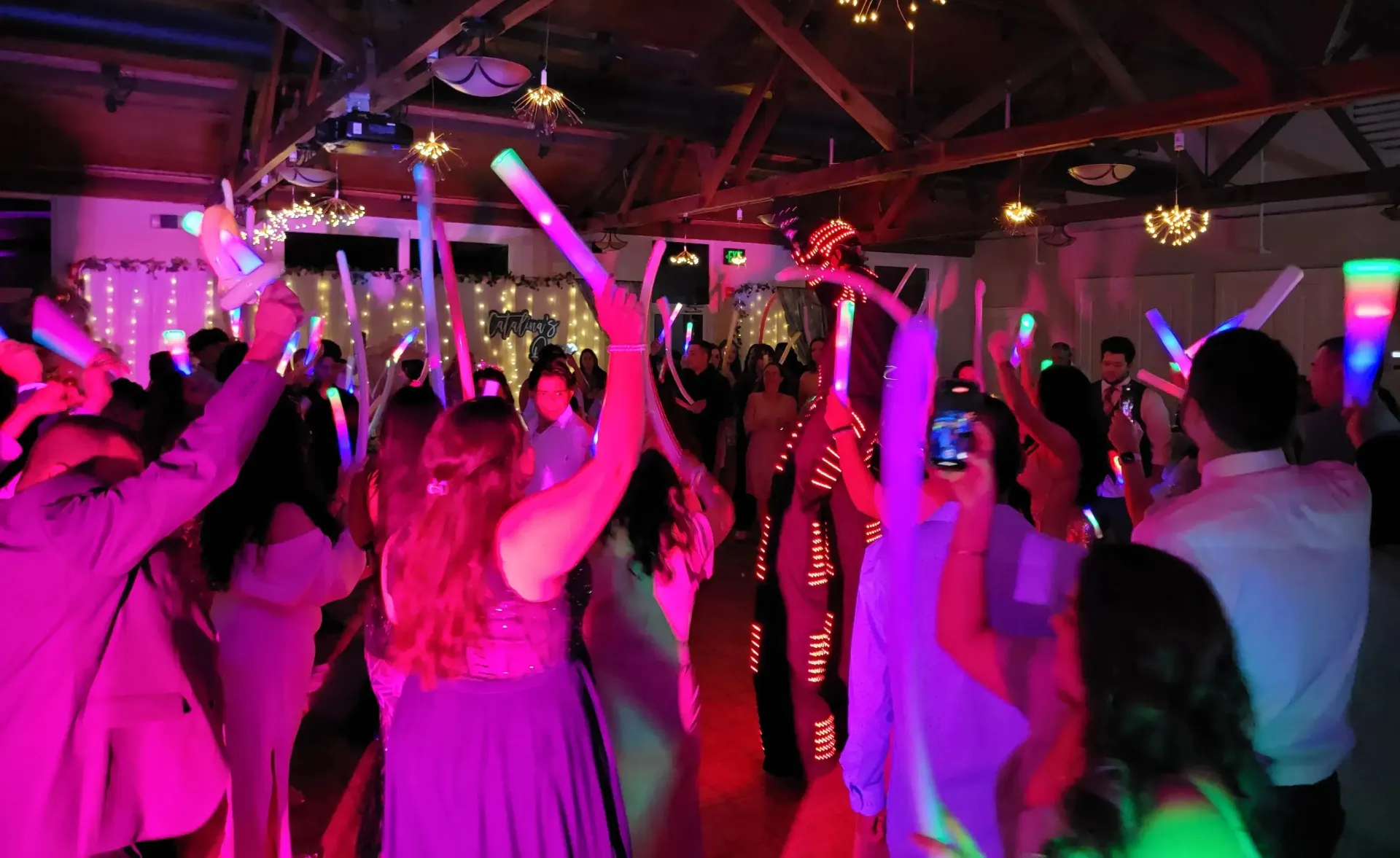 Crowd dancing in a nightclub under bright pink and purple lights, arms raised.