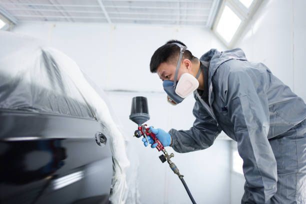 A man wearing a mask is spray painting a car.