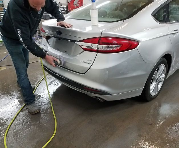 A man is polishing the back of a silver car