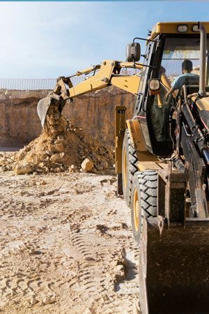 Yellow backhoe dumping dirt at a construction site, blue sky background.