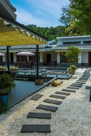 Pathway of stepping stones leads to a building with a yellow awning and patio seating, surrounded by a white gravel yard.