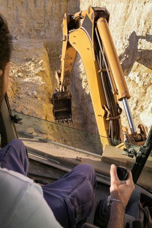 Man operating a yellow excavator digging in a trench.