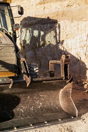 Bulldozer next to a sand-colored earth wall, under sunlight.