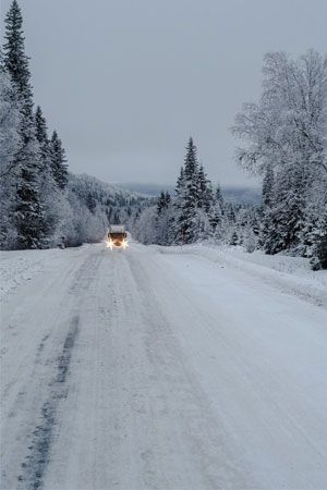 Snowy road Snowy road through a forest with a car driving towards the viewer; overcast sky.