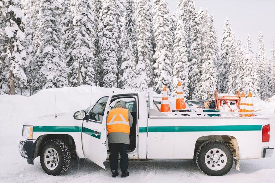 Person in safety vest getting out of a white truck in a snowy forest.