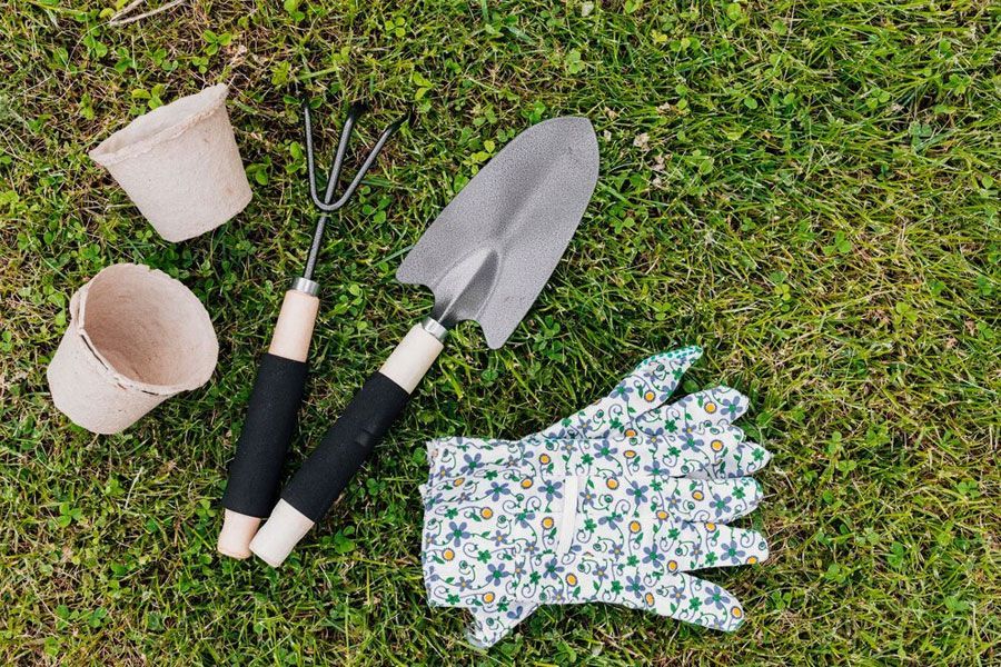 Gardening tools (trowel, hand rake, gloves, pots) on green grass, ready for planting.