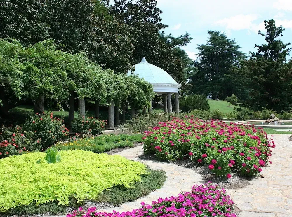 Scenic garden with gazebo, flowers, and lush greenery under a blue sky.