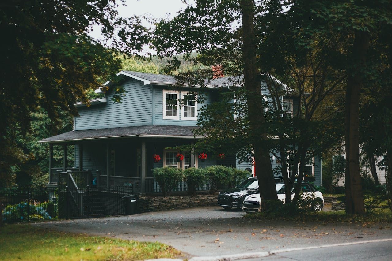 Blue house with porch, trees, and driveway; car parked in front.