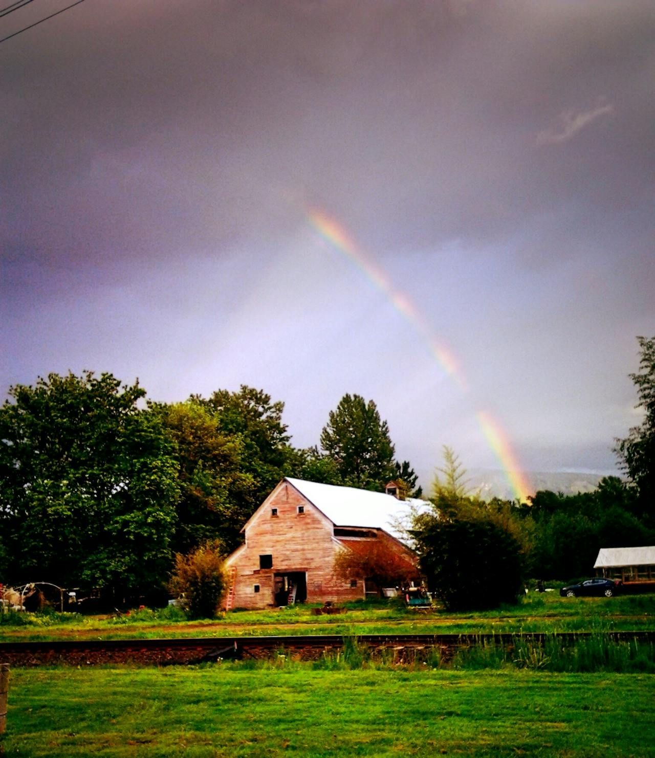 Barn with rainbow over a green field, dark clouds in the sky.