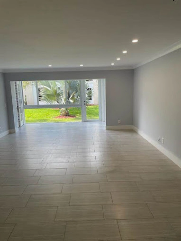 Empty room with large window overlooking green lawn and palm tree; grey walls, light wood floor.