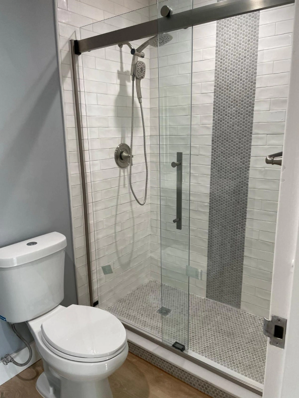 Modern bathroom with a glass shower, white toilet, and gray and white tiled walls.