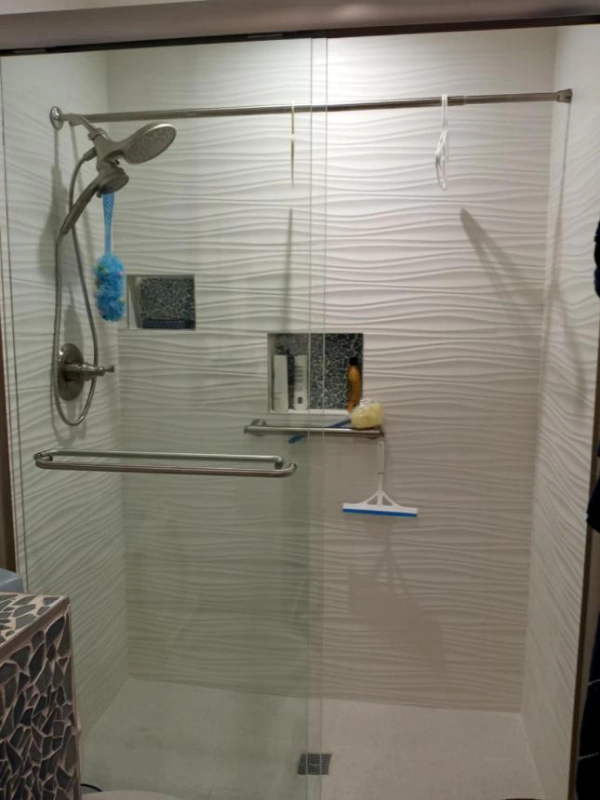 Glass-walled shower with textured white tile and brushed nickel fixtures, including a hand-held showerhead.