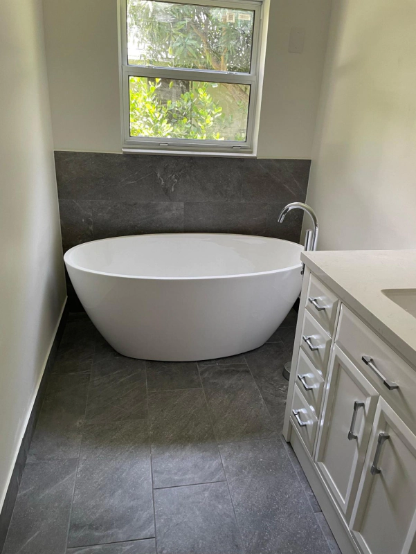 Modern bathroom with a white soaking tub, grey tile, and a white vanity.