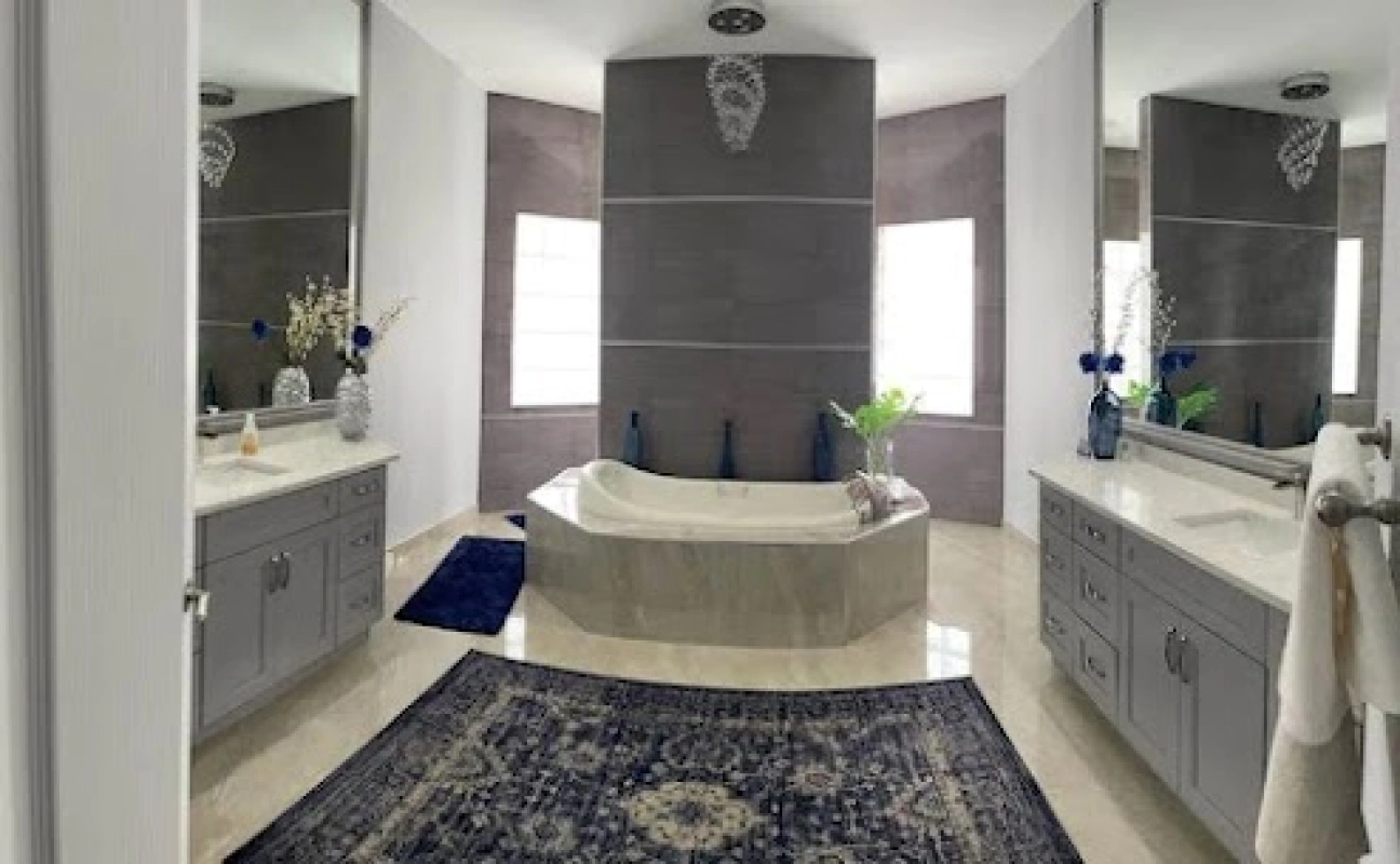 Luxurious bathroom with gray cabinets, marble floor, a tub, and two mirrors. Blue rug.