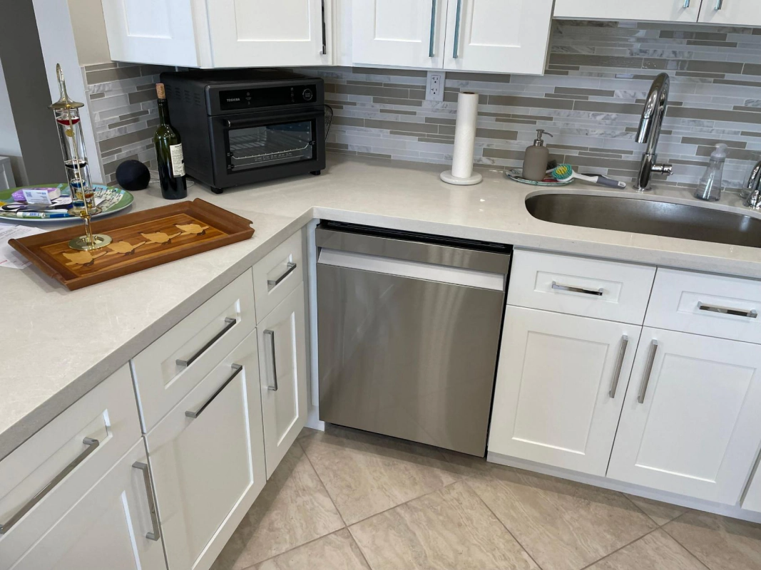 A modern kitchen with white cabinets, stainless steel dishwasher, and a sink.