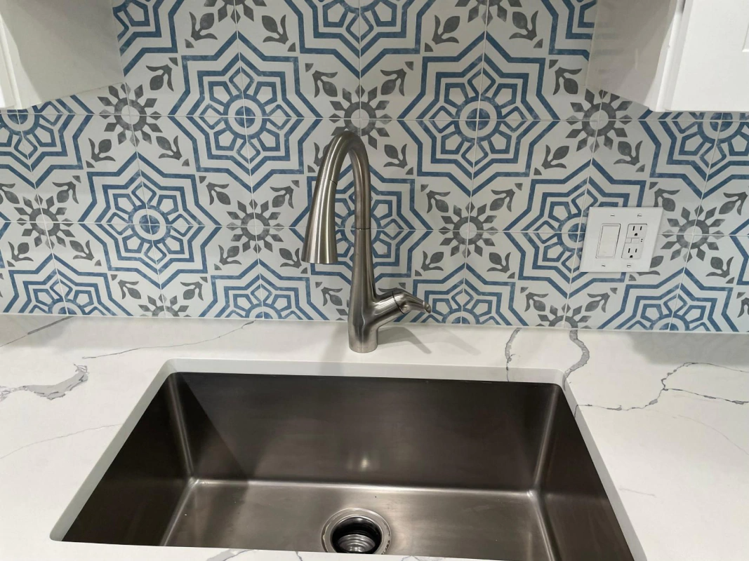 Stainless steel kitchen sink with a patterned tile backsplash and faucet.