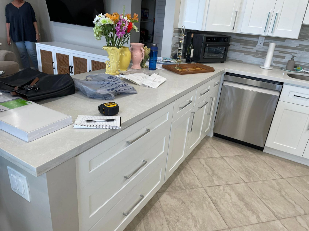 Kitchen with a white countertop, cabinets, and appliances. Flowers and items rest on the counter.