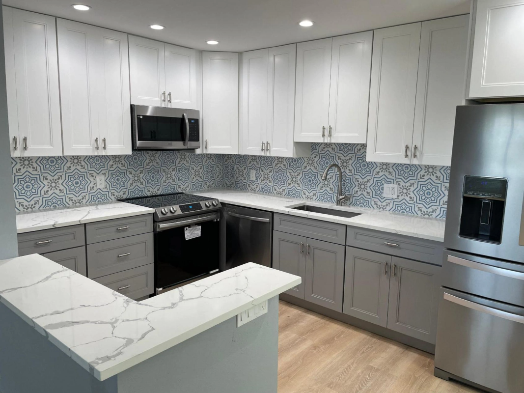 Modern kitchen with white and gray cabinets, blue patterned backsplash, stainless steel appliances, and light wood floors.