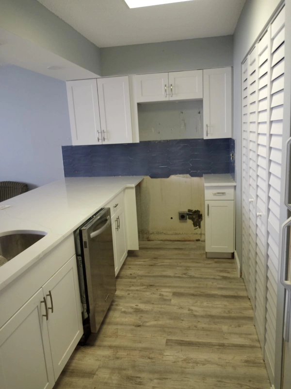 Modern kitchen with white cabinets, stainless steel appliances, and wood-look flooring.