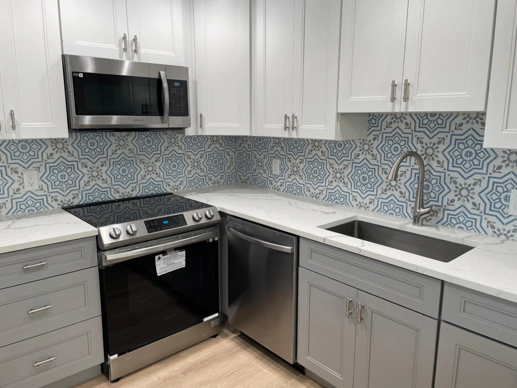 Modern kitchen with white and gray cabinets, stainless steel appliances, and blue patterned backsplash.