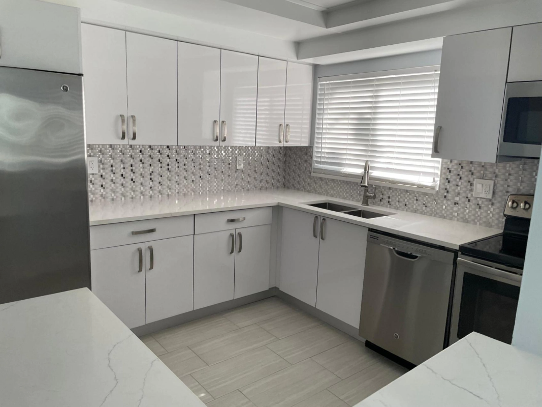 Modern white kitchen with stainless steel appliances and backsplash.