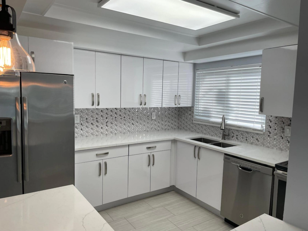 Modern white kitchen with stainless steel appliances, white cabinets, and a patterned backsplash.