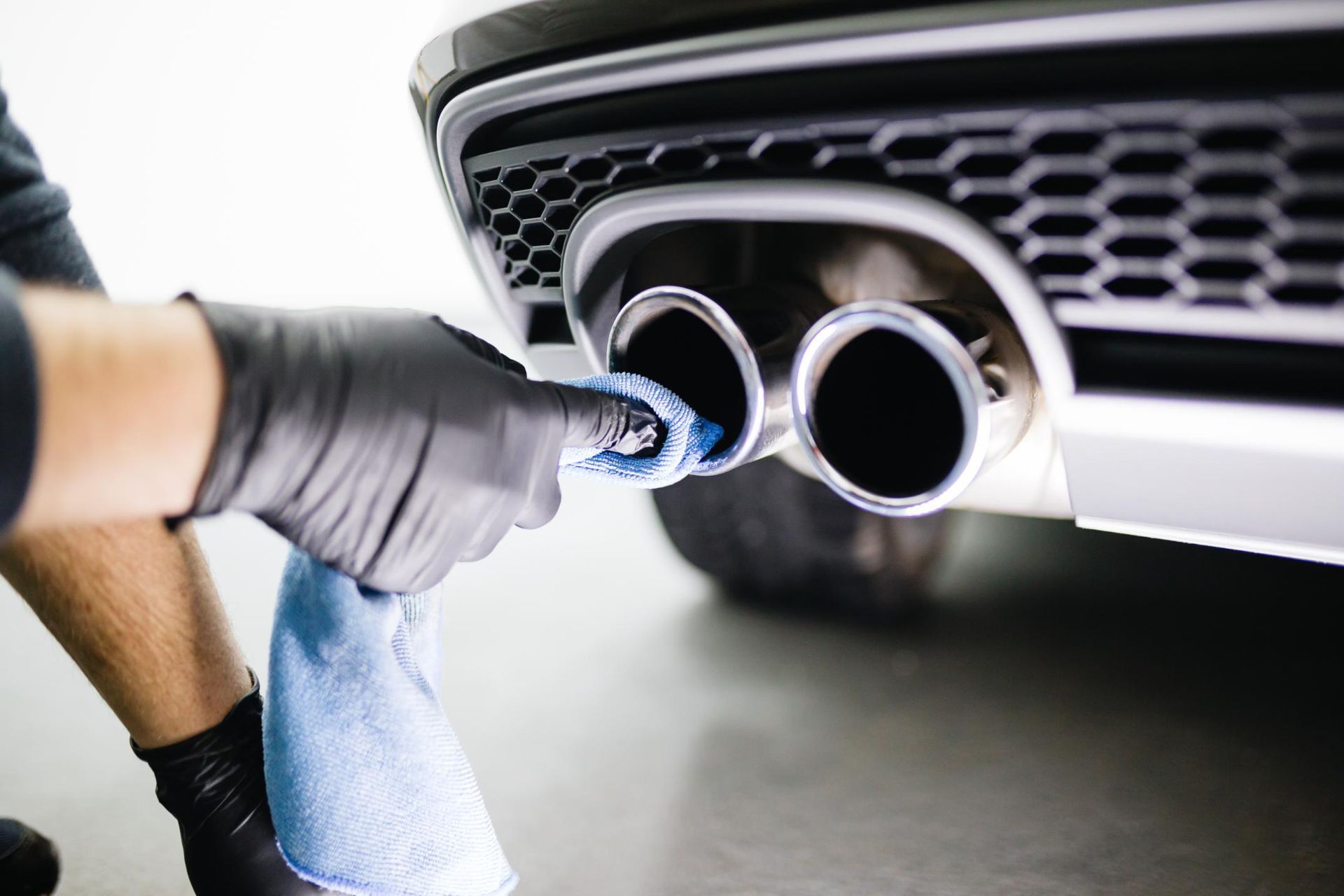 A person is cleaning the exhaust pipe of a car with a towel.