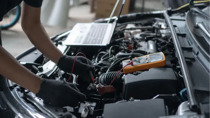Person working in a car engine bay with tools and an orange battery pack