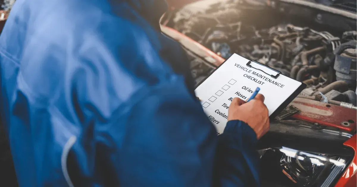Person writing on a clipboard while standing near an open car engine.