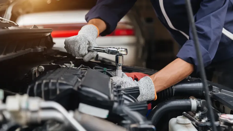 Mechanic wearing gloves working under a car hood with engine components visible