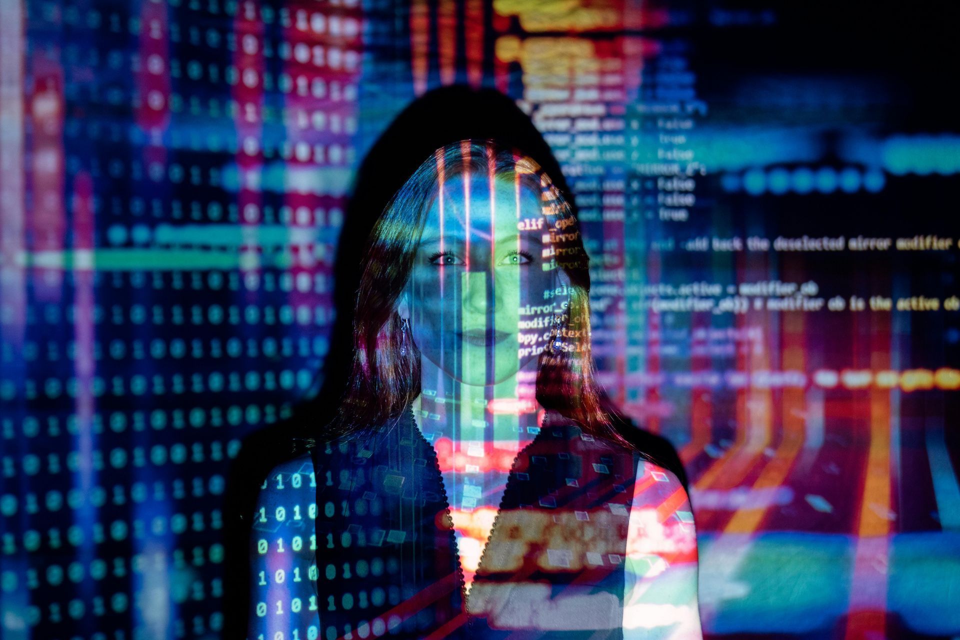 A woman is standing in front of a computer screen with binary code.