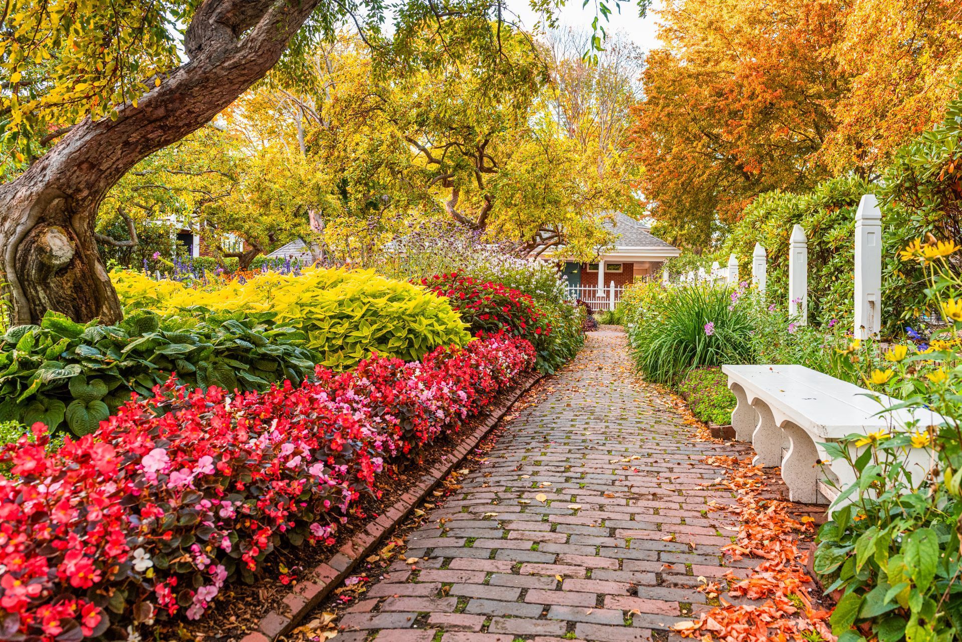 A brick path in a garden with flowers and a bench.