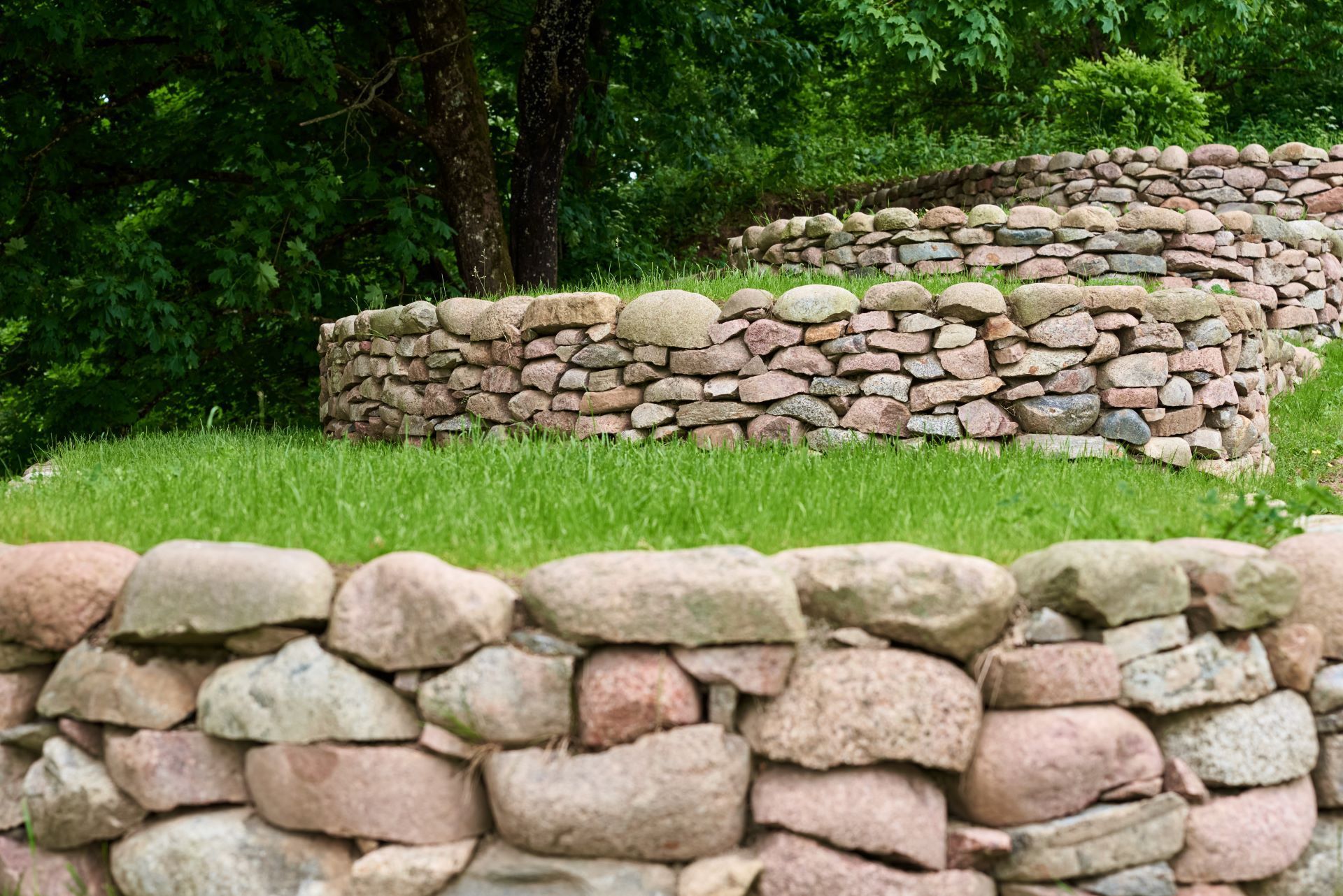 A stone wall is surrounded by grass and trees in a park.