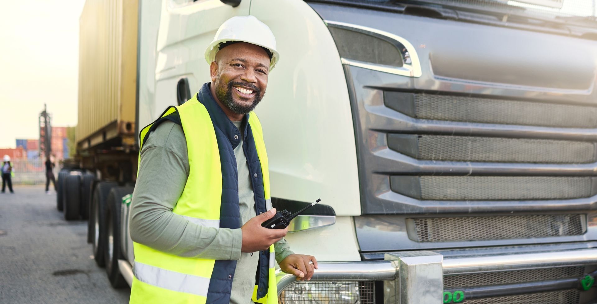 A man in a yellow vest is standing in front of a truck holding a tablet.