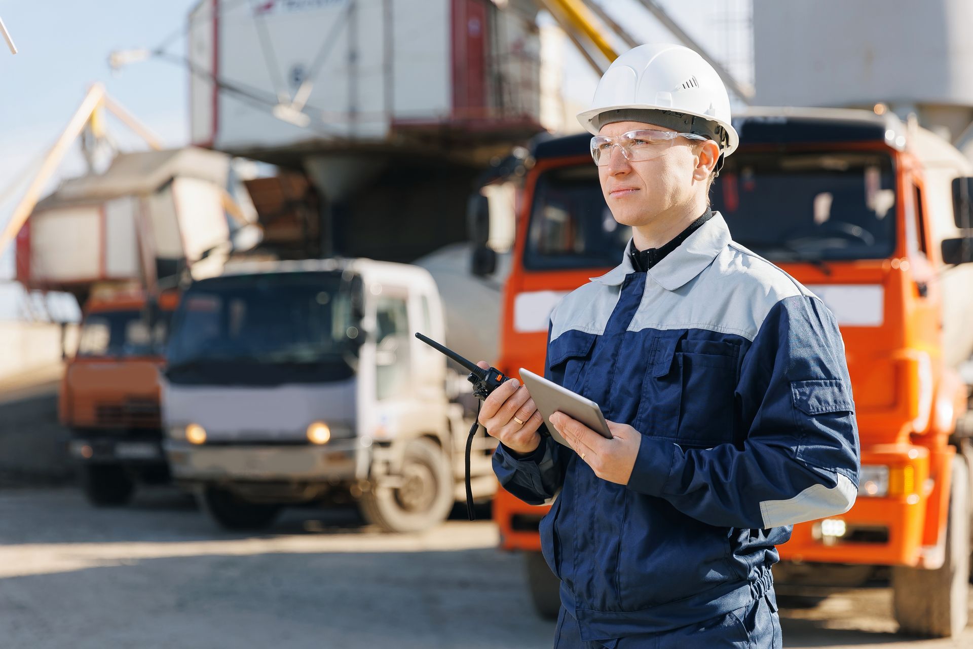 A man is standing in front of a row of trucks holding a tablet and a walkie talkie.